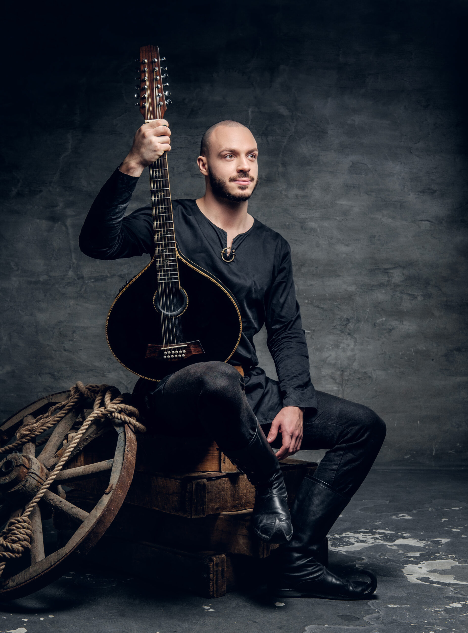 Studio portrait of traditional folk musician dressed in vintage Celtic clothes sits on a wooden box and holds mandolin.